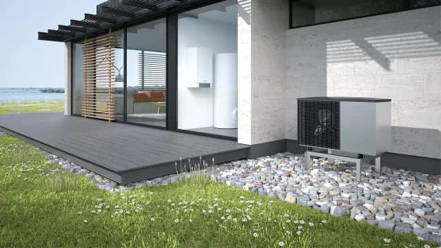 Groupe extérieur de pompe à chaleur Viessmann posé sur un support au pied d’un mur clair, sur un lit de galets, à côté d’une terrasse en bois